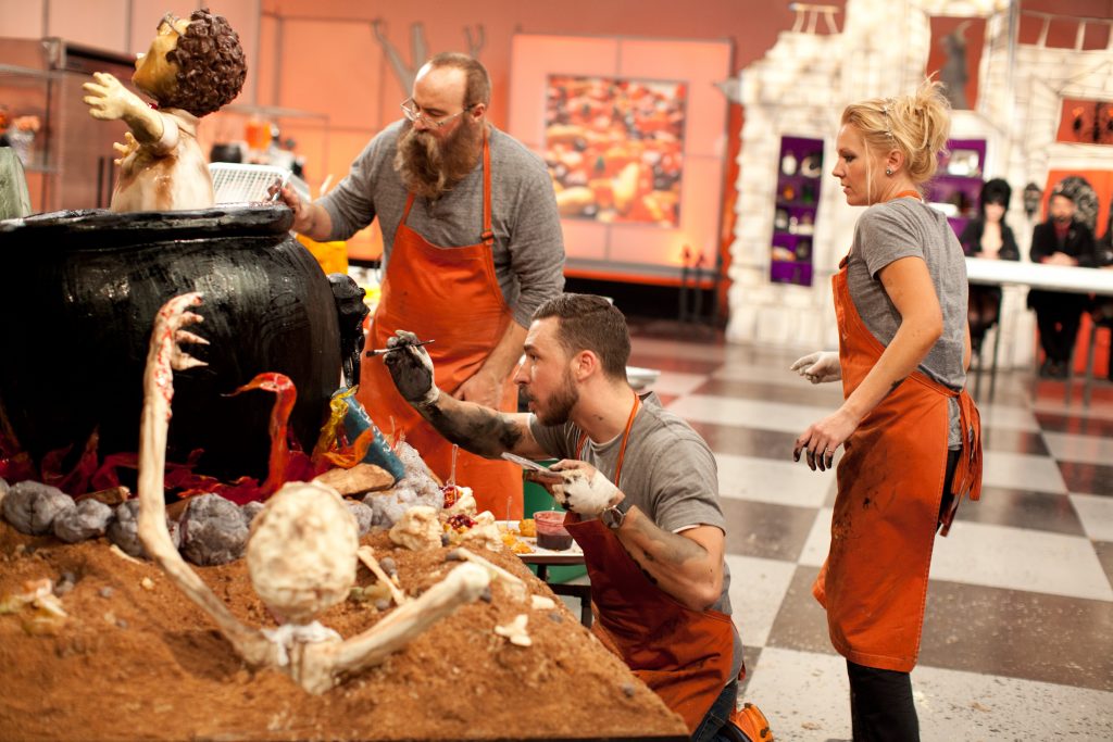 The Orange team's Adam Bierton, middle, Darci Rochau, right, and Robert Teddy, left, put the finishing touches on their creation during the final "spine chiller" challenge, as seen on Food Network's Halloween Wars, Season 5.